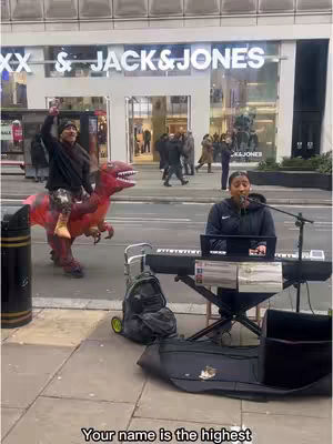 A street scene with a woman singing and playing keyboard, framed in front of a Jack & Jones store. Another man in a dinosaur costume rides a red inflatable dinosaur in the background.