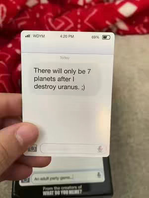 A hand holds a white card displaying a mock text message conversation. The background is a blurry red and white pattern. The card looks like a phone screen, and the text reads a humorous message.