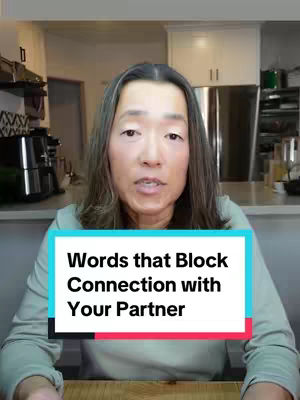 A medium shot of a woman in a home setting, looking directly at the camera. She has long, straight gray hair and is wearing a light green long-sleeved shirt. In front of her is a rectangular text overlay reading, "Words that Block Connection with Your Partner." The background consists of a kitchen, with white cabinets visible behind her.