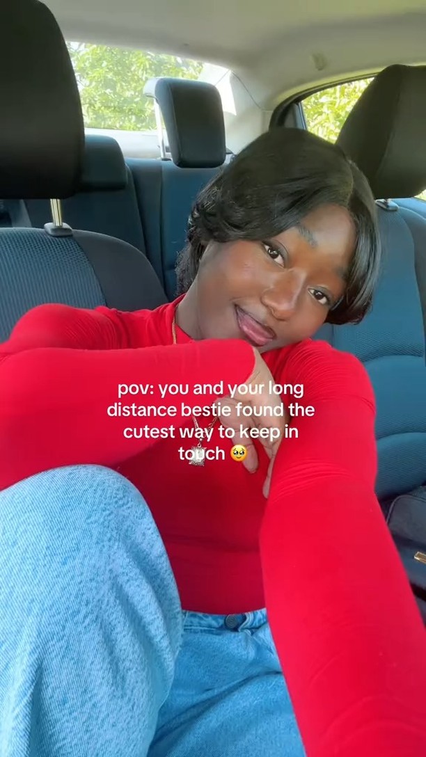 A person, wearing a red top, is seated inside a car. Overlaid text is present, and the person is smiling. The car's interior, including the headrests and seats, is visible in the background. The person is looking towards the camera.