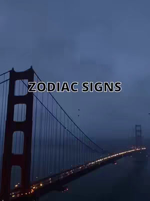The Golden Gate Bridge is shown in the image, with a slightly overcast and moody sky as a backdrop. The bridge arches gracefully from left to right, and lines of lights illuminate the bridge's deck, suggesting vehicles are traveling across. The text 'ZODIAC SIGNS' is superimposed on the image. Overall, the image has a cool, muted color palette.