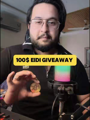 A man with glasses holding a coin in front of a microphone, with a yellow text box overlaying the image reading \".\".