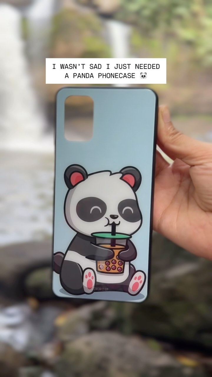 A hand holding a phone case featuring a cartoon panda drinking bubble tea. The background is a blurred image of a waterfall and surrounding foliage.