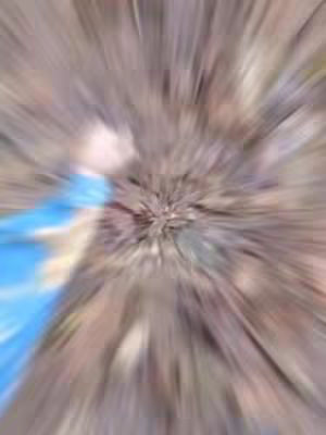 The image is abstract with a radial blur effect. Various shades of brown and tan dominate the composition, with lighter streaks emanating from a central point. A splash of blue is visible in the bottom left corner, seemingly out of focus, while the rest of the image is deliberately blurred.