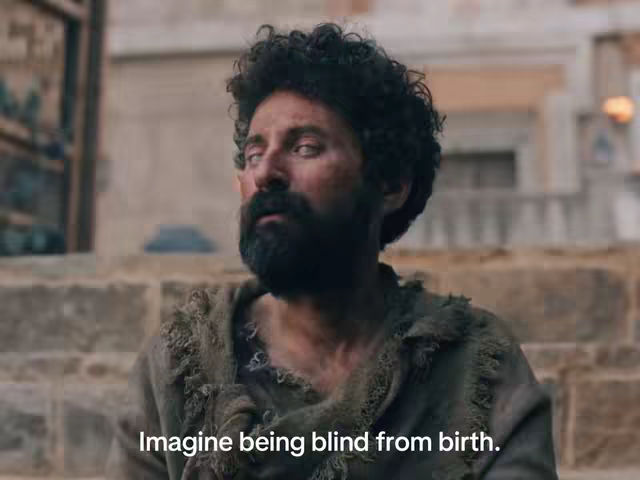 The cover image features a medium shot of a man with dark curly hair and a full, dark beard. He wears rough, tattered clothing. The man has a sorrowful expression and seems to be looking off to the side with whitened eyes, suggesting blindness. The background is blurred, but it seems to be outdoors