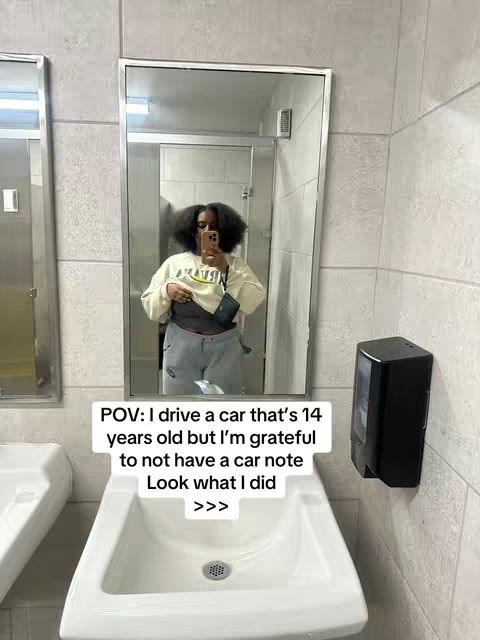 A person is taking a selfie in a public restroom. The person is reflected in the mirror, which also shows the sink and other restroom features. Text overlay states a relatable message about a car.