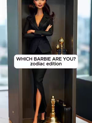 The image presents a Barbie doll inside a display case. The doll is dressed in a sleek, black business suit. The background is a blurred view of an office setting. A text overlay informs viewers "WHICH BARBIE ARE YOU? zODIAC EDITION."
