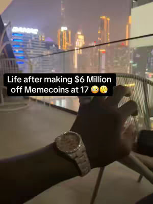 A hand with a diamond watch is held up in front of a blurred, nighttime cityscape, with lights from buildings and structures.