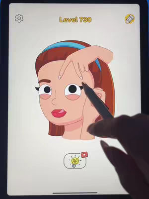 The cover image shows a cartoon illustration of a woman's face on a white background. A hand is shown holding a pen, appearing to interact with the image on a digital device or screen. The woman's image displays in a white screen. The woman is fair-skinned, with brown hair, and a blue headband. The illustration also features large eyes, and red lips. The screen has a lightbulb icon with a play button on the bottom.
