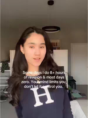 A young woman with long dark hair is centered in the frame, the background blurred. She wears a navy blue sweater with a large white 'H' on it. Text overlayed on the image reads: 'Some days I do 8+ hours of revision & most days zero. Your mind limits you, don't let it control you.'