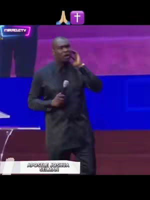 A man with a microphone stands on a stage, speaking with a hand near his ear as if listening or emphasizing his words. The background is brightly lit with purple, blue, and white hues, and the video appears to be of a religious service.