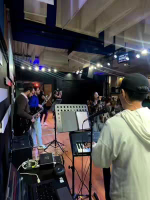 The cover image shows a band performing on stage. The focus is from the perspective of someone playing a keyboard, with a microphone in front of them. Other band members are visible in the background, including a guitarist and a singer. The lighting is bright, highlighting the band members and instruments. The layout includes a stage setup with musical equipment. The overall composition is a live performance scene.
