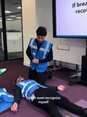 The cover image shows a medical training scenario inside an office setting. One man, dressed in a reflective vest, kneels beside another lying on the floor, with a presentation screen in the background.