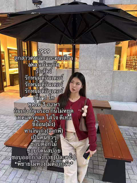 A woman stands beneath a large black umbrella. She is wearing a red cardigan, a white top, and light-colored pants. Text overlays are present, describing her. The background shows a building with windows and a wooden bench.