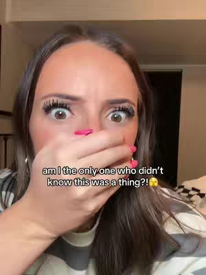 A close-up shot focuses on a woman's face, hands covering her mouth in a surprised expression, captured against a blurry indoor setting.