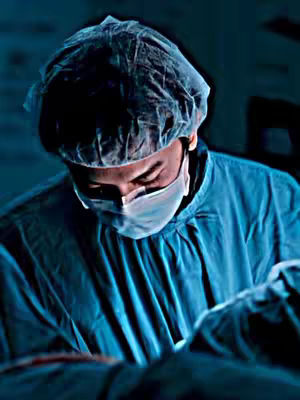 The cover image shows a close-up view of a person, likely a medical professional, wearing surgical attire in a dimly lit environment. The person is wearing a surgical cap and a face mask, obscuring most of their face. The person is focused on what appears to be a medical procedure. The lighting is dark and seems to be coming from above and behind the person, creating shadows and highlighting the surgical attire and the details of the face mask and cap.