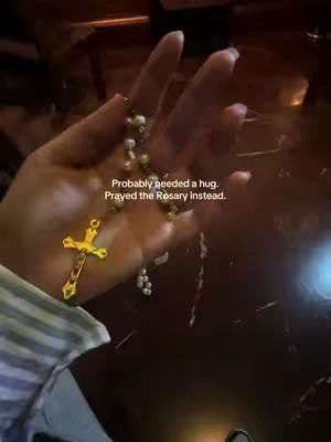 A hand holding a rosary with a gold crucifix against a blurred background. Text overlays the image.