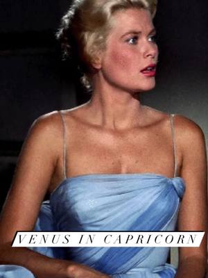 A still image from a movie, showing a woman with blonde hair looking off to the side with a concerned expression. She is wearing a light blue dress with a gathered neckline and spaghetti straps. The text 'VENUS IN CAPRICORN' is overlaid on the bottom of the image in a white banner.