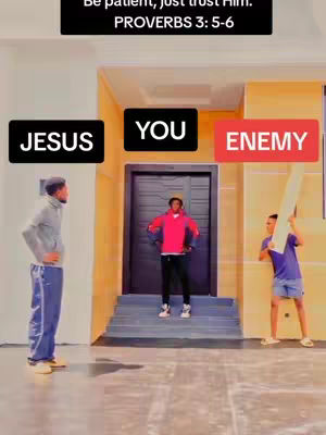 The image is a staged scene with three men. One stands to the left in a gray jacket and blue track pants, with his arms at his sides. In the center is a man in a red hoodie, black pants, and sneakers, arms at his sides. To the right, another man holds a white board, wearing a blue shirt. Text boxes label the men 'JESUS', 'YOU', and 'ENEMY'. The background shows an architectural setting.