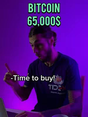 A man with dark hair and a beard points his finger at the viewer with a surprised expression. Text overlay reads, 'BITCOIN 65,000$' in green font. Below the man is text that says, '-Time to buy!' in white font. The man is wearing a dark blue t-shirt with a logo. The background is purple.