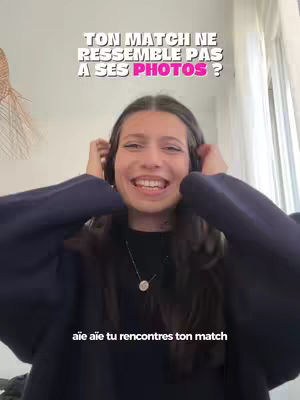 A young woman with long dark hair smiles, holding her hands up near her head. Overhead, a white text overlay asks, "TON MATCH NE RESSEMBLE PAS A SES PHOTOS ?" (Your match doesn't look like his photos?). Beneath, the text "aïe aïe tu rencontres ton match" (ouch, ouch you meet your match) is visible. The background is blurred, and a decorative hanging element is seen at the left, with what seems to be a window on the right providing natural light.