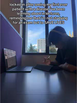 The image presents a study desk scene with a person sitting at it, angled from the side. The person is hunched over, absorbed in work or study. A laptop and a tablet rest on the dark desk surface. Light from a window brightens the right side of the image, and text overlays are present, making the image informative. The background reveals a window showing an outdoor scene.