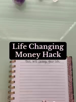 The image showcases a notebook open to a blank page with a spiral binding. The notebook rests on what appears to be a light green surface, with some crystals and other decorative elements slightly visible in the background. A black banner with white text overlays the notebook.