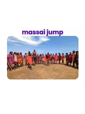 The image shows a group of people, likely of African descent, standing in a circle on a dirt ground under a bright blue sky with some clouds. They are dressed in various colorful traditional garments, including what appear to be red and patterned cloths draped over their shoulders. A text overlay in purple, stating "massai jump", is present at the top-center of the image, set against the bright sky. The composition is wide, focusing on the circle of people and the open environment, with a high-angle perspective.