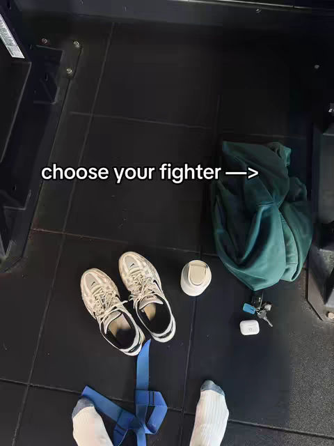 An overhead perspective shows a gym floor with sneakers, a hoodie, and accessories next to the feet of the person in the frame. Text overlay says 'choose your fighter'.