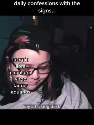 The cover image presents a person indoors with a background that appears dark. A person is facing the camera partially, wearing glasses and a black cap. The image includes overlaid text listing zodiac signs and an additional line: "buy a f*cking desk."