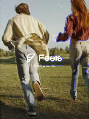 The image shows two people running away from the camera in a field. The person closer to the camera is wearing light-colored jeans and tan shoes. The person in front wears a yellow button-down shirt and light-colored jeans. A purple logo and text overlay stating 'Feels Strictly under 30' is center in the image.
