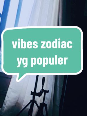 A vertical image with a teal speech bubble overlaid on a blurred background. Inside the speech bubble, white text reads 'vibes zodiac yg populer'. The background is a curtained window with a tripod in the foreground.