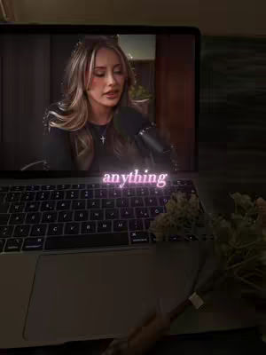 A woman appears on a laptop screen within a dimly lit setting. The text overlay "anything" is in a glowing pink font.