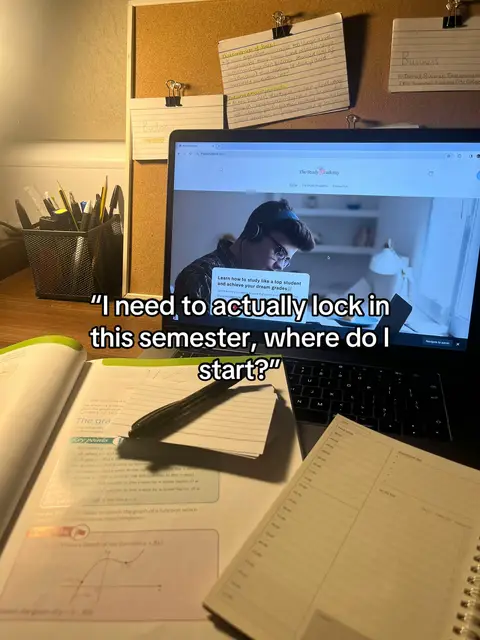 A desk setup with a laptop, a notebook, and textbooks. The laptop screen shows a website with a person wearing headphones. A note is taped to the wall behind the laptop. The colors are muted with brown and white tones.