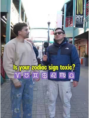 Two men stand on a street corner. The man on the left is wearing a light-colored sweater and jeans, while the man on the right wears sunglasses and a jacket. Text overlay features, 'Is your zodiac sign toxic?' and a row of zodiac symbols.