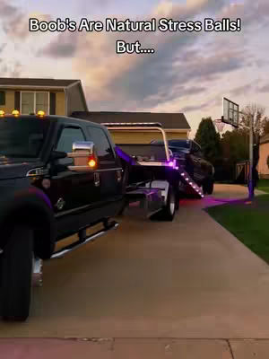 The cover image shows a black tow truck parked on a driveway. The truck is angled towards the left, and a second vehicle is being towed behind it. The background features a house, trees, and a basketball hoop standing on the right. The sky is cloudy.