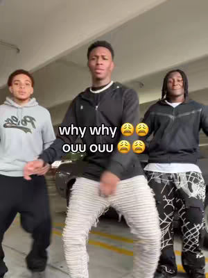 Three young men are dancing in an indoor parking garage, wearing casual clothing. The text overlay says 'why why' followed by several crying face emojis and then 'ouu ouu' with more crying face emojis. The center subject is wearing a black jacket with a white shirt and off-white pants, while others are in a grey hoodie and black pants and a black hoodie and patterned pants.