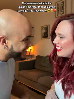 The cover image shows a man and a woman in a close-up, facing each other and smiling. The woman has long red hair and is wearing a white top. The man is bald and has a beard. They are in a room with neutral-toned decor and a couch.