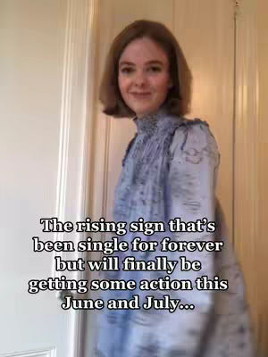 A woman with light brown hair is seen from the chest up, standing in a room with white framed doorways. She's wearing a light blue dress. The overlaying text reads 'The rising sign that's been single for forever but will finally be getting some action this June and July...'