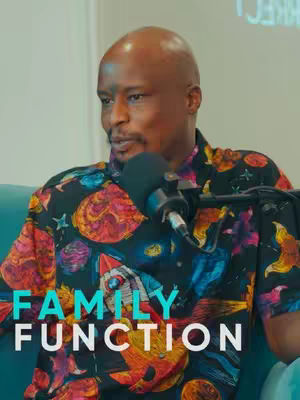 A close-up shot features a man with a shaved head, smiling slightly while speaking into a microphone. He is wearing a colorful, patterned shirt with prominent text overlaying the lower part of the image that reads 'FAMILY FUNCTION'. The backdrop is a neutral, possibly off-white wall.