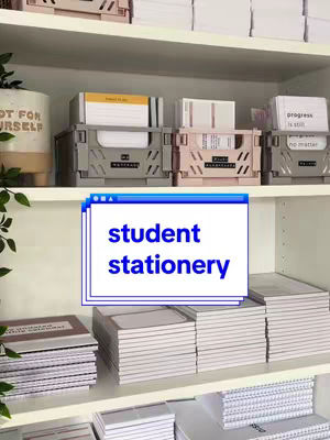 A well-organized shelf displays a variety of stationery items, including notebooks, index cards, and storage boxes. The shelf is white, and the items are in neutral colors, creating a sense of calm and order.