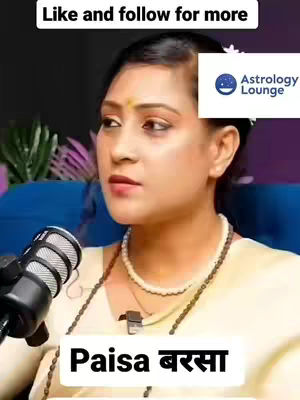 A woman in a cream-colored top is speaking into a microphone. The background is blurred but appears to be an interior space, with some plants visible. A text box at the bottom reads "Paisa バ サ" in Devanagari script.