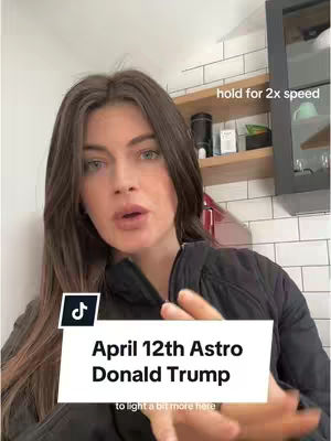 A woman with long, dark hair is centered in the frame, slightly facing the camera. She's wearing a black top. Behind her is a domestic kitchen setting with white-tiled walls. The overlay text reads, 'April 12th Astro Donald Trump'.