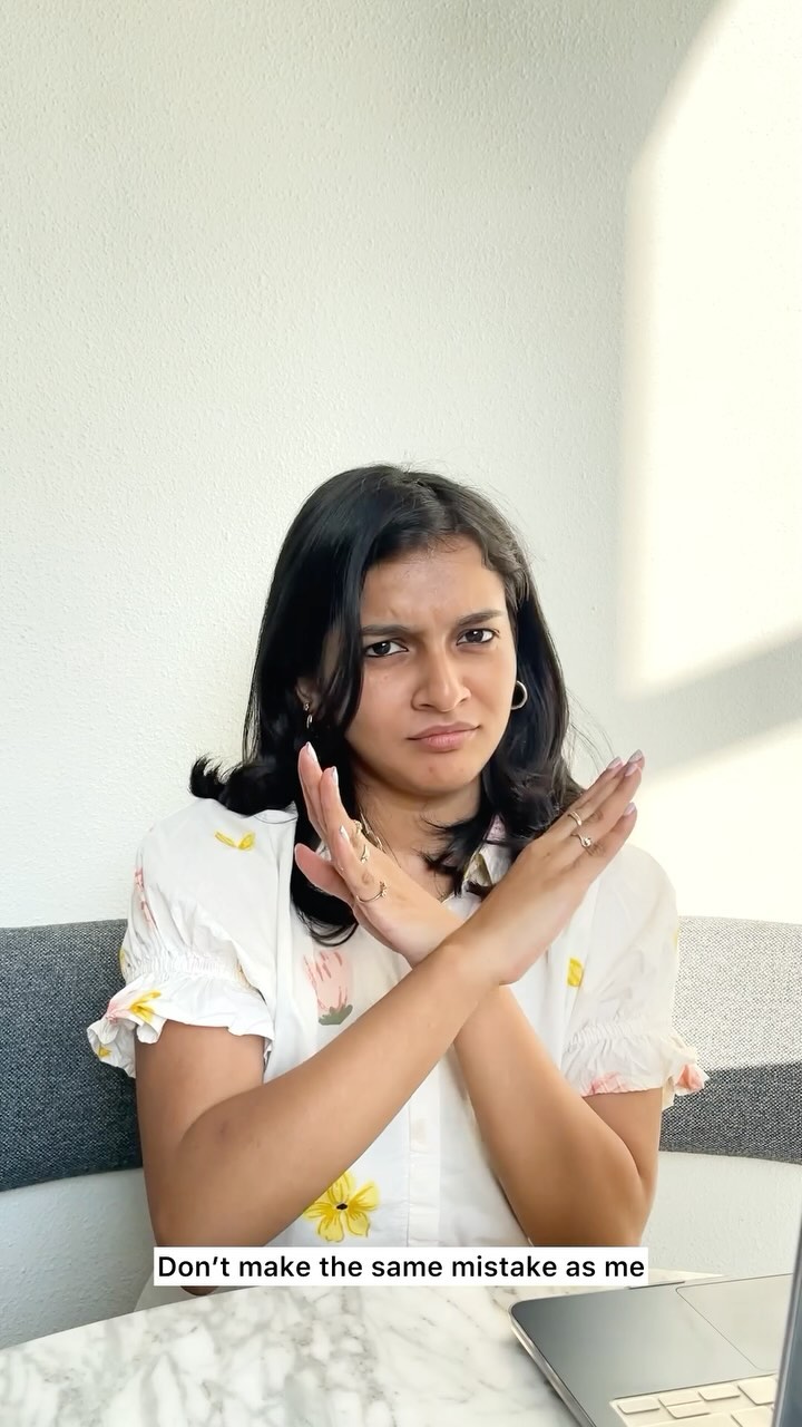 A woman is in the frame with her arms crossed in front of her, in a gesture of negation. She wears a patterned white top, and the background is a plain white wall. There is text at the bottom of the image.