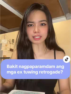 A young woman with long, dark hair is the central focus, facing slightly towards the camera and speaking. She wears a black spaghetti-strap top. Behind her, the background suggests an indoor setting with what might be wooden panels or a wall, and some soft lighting. An overlay in the lower-left features text in a rounded rectangle. A music note icon is visible in the top-right.
