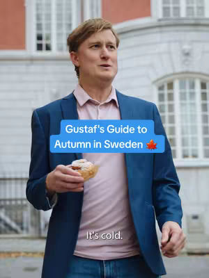 A man in a blue blazer and pink shirt holds a pastry in front of a building. A blue box on the image states 'Gustaf's Guide to Autumn in Sweden'. Below the box, the text says 'It's cold.'