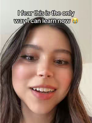 A close-up shot of a young woman with dark hair and fair skin. Text overlayed at the top reads, 'I fear this is the only way I can learn now,' accompanied by a crying emoji. The woman is looking towards the right of the frame with a slight smile, her mouth open. Soft lighting and neutral background. The overall composition suggests a vlog or selfie-style video.