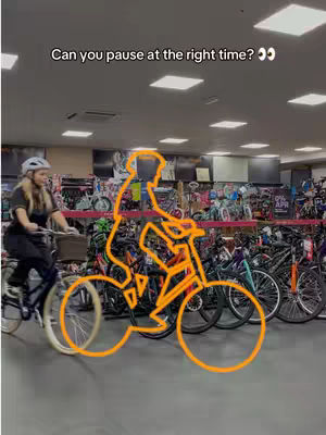 A person riding a bicycle in a bike shop, with the image overlaid with an orange outline of a person and bicycle and text at the top saying, "Can you pause at the right time?" The background shows more bikes and retail displays.