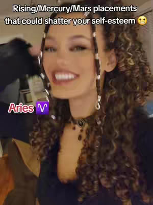 A selfie-style video cover shows a woman with curly hair, smiling widely. She is wearing a dark top and a beaded choker necklace. Text overlays advertise the video's theme, with an astrological sign symbol over her chest.