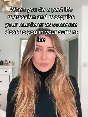 A woman with long blonde hair is centered in the frame, looking directly at the camera with a neutral expression. She is wearing a black turtleneck, and the background includes glimpses of a white dresser and a doorway. Text overlayed on the image reads a statement about recognizing someone close to you as your murderer in a past life regression.